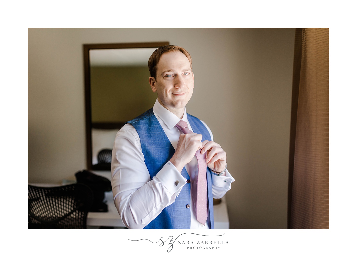groom adjusts pink tie in navy suit and vest