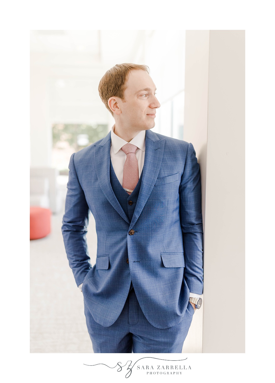 groom poses in blue suit with pink tie
