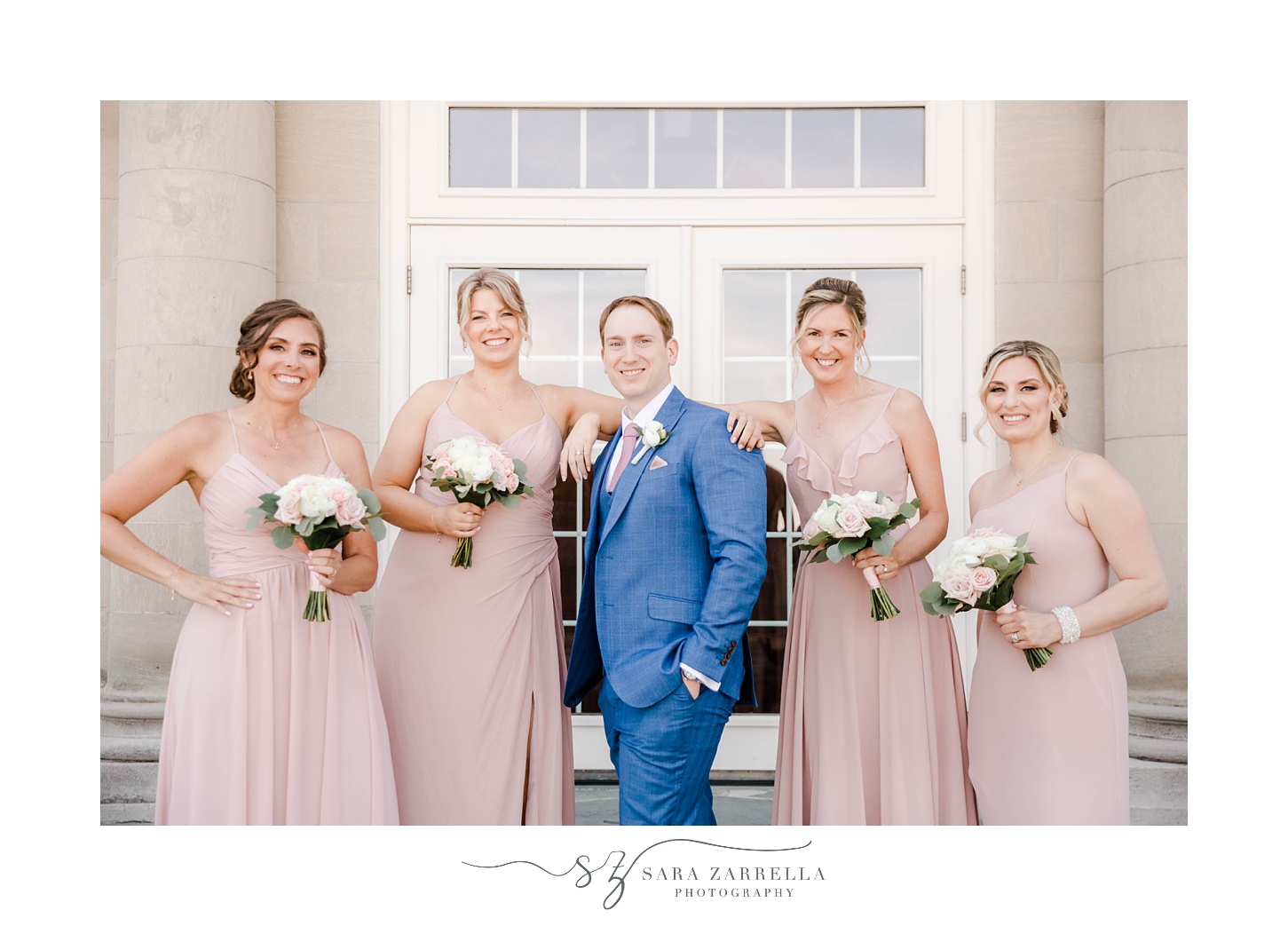 groom poses with bridesmaids in pink gowns on steps of Aldrich Mansion