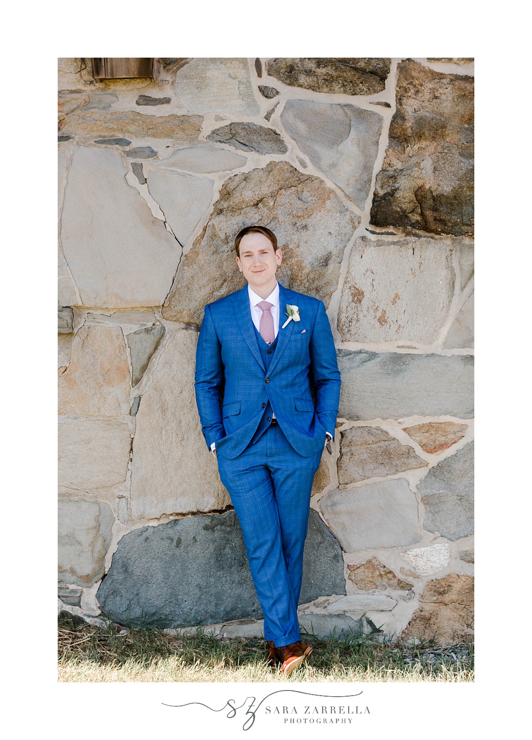 groom leans against stone wall at Aldrich Mansion in blue suit 