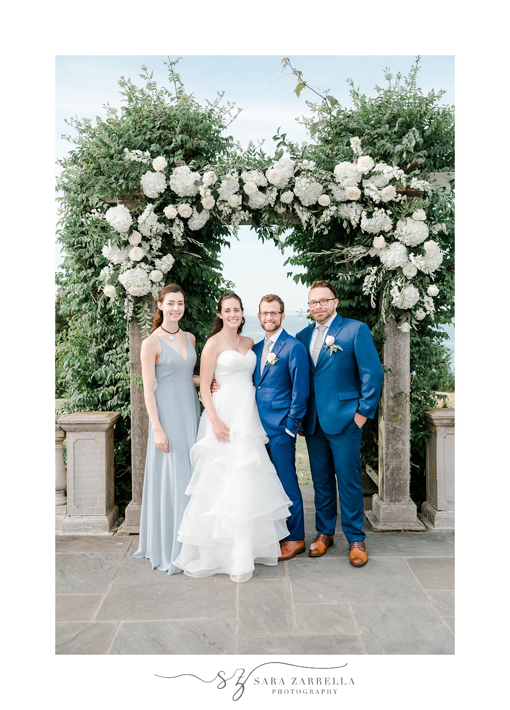 newlyweds stand with wedding party under floral arch at Castle Hill Inn
