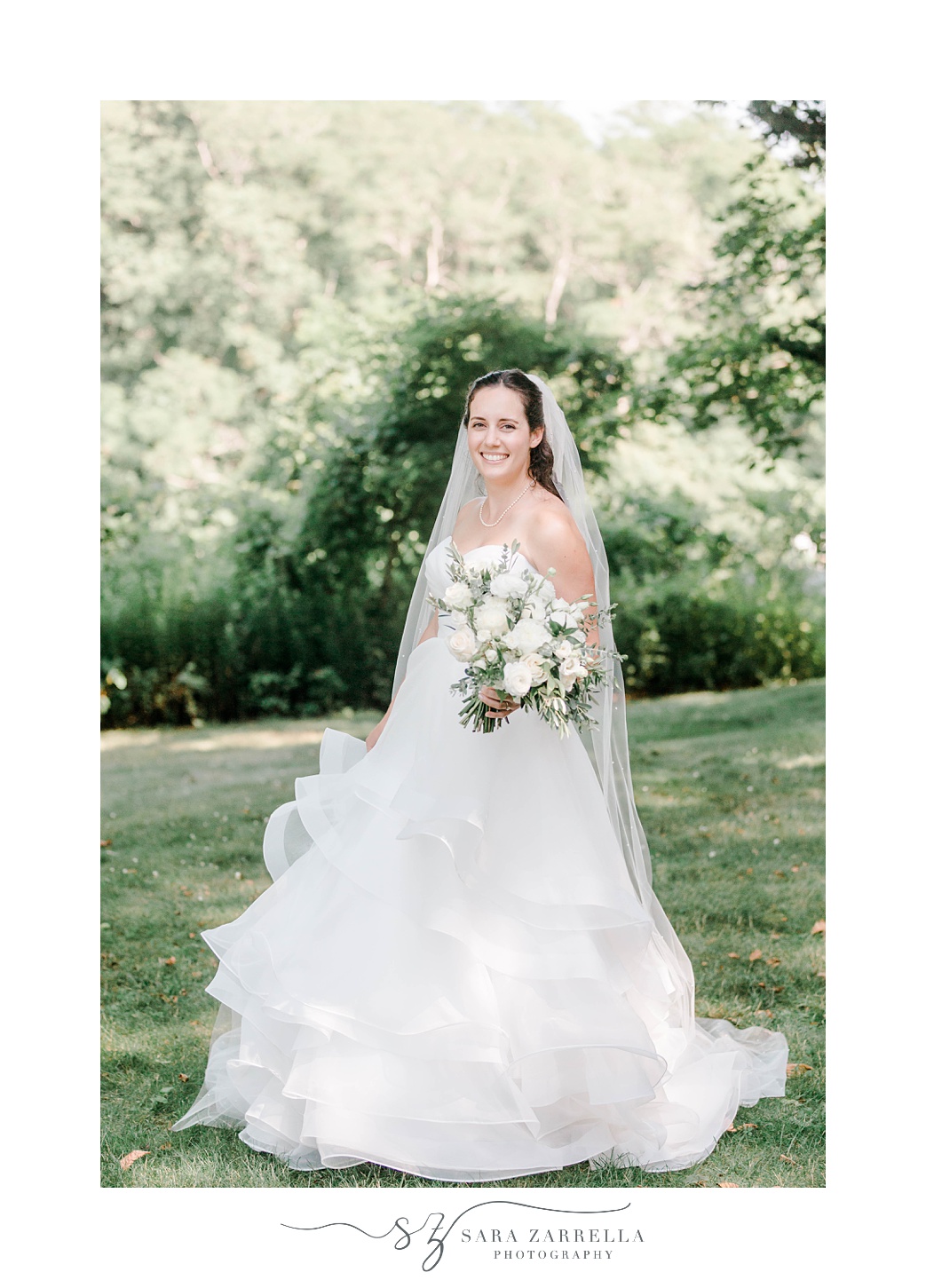 bride stands in classic wedding gown with veil around shoulders 