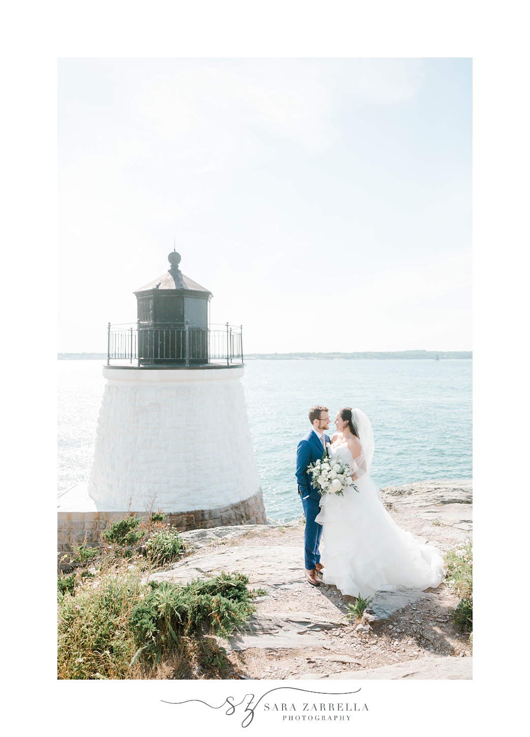 newlyweds stand together by lighthouse in Rhode Island 