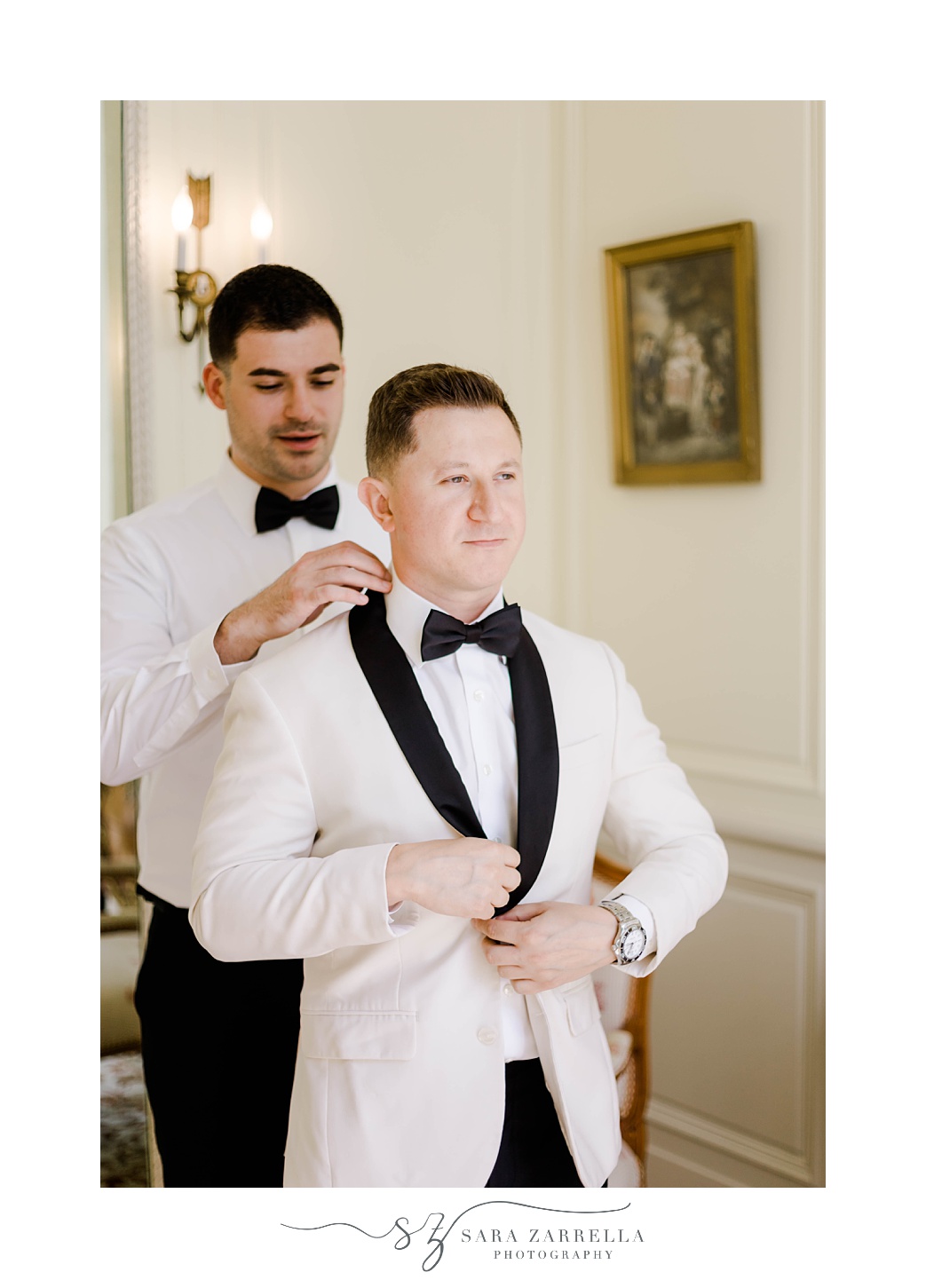 groomsman helps groom adjust white tux jacket 