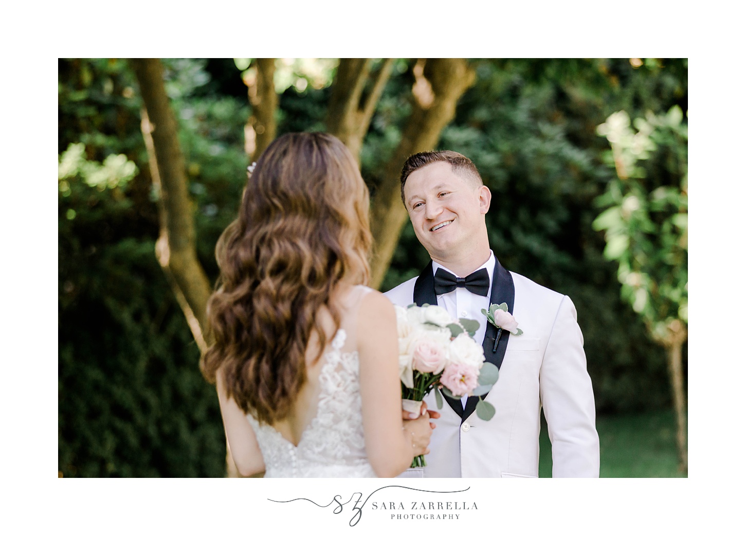 groom in white tux jacket smiles at bride during first look