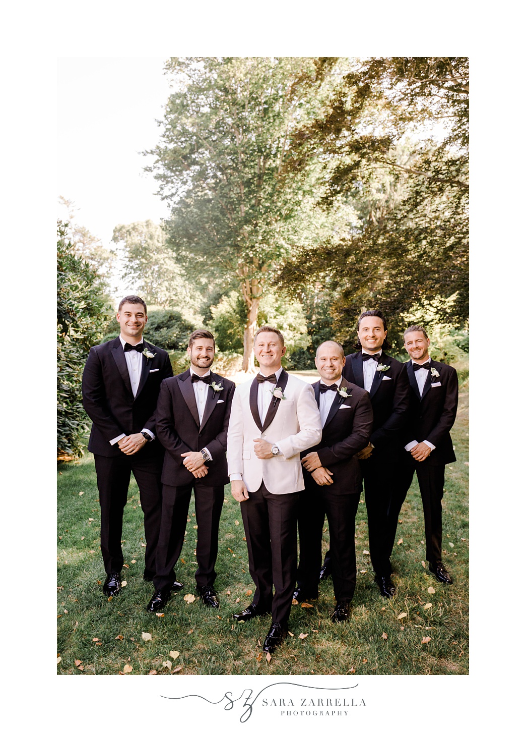 groom in classic white tux jacket poses with groomsmen in black suits 