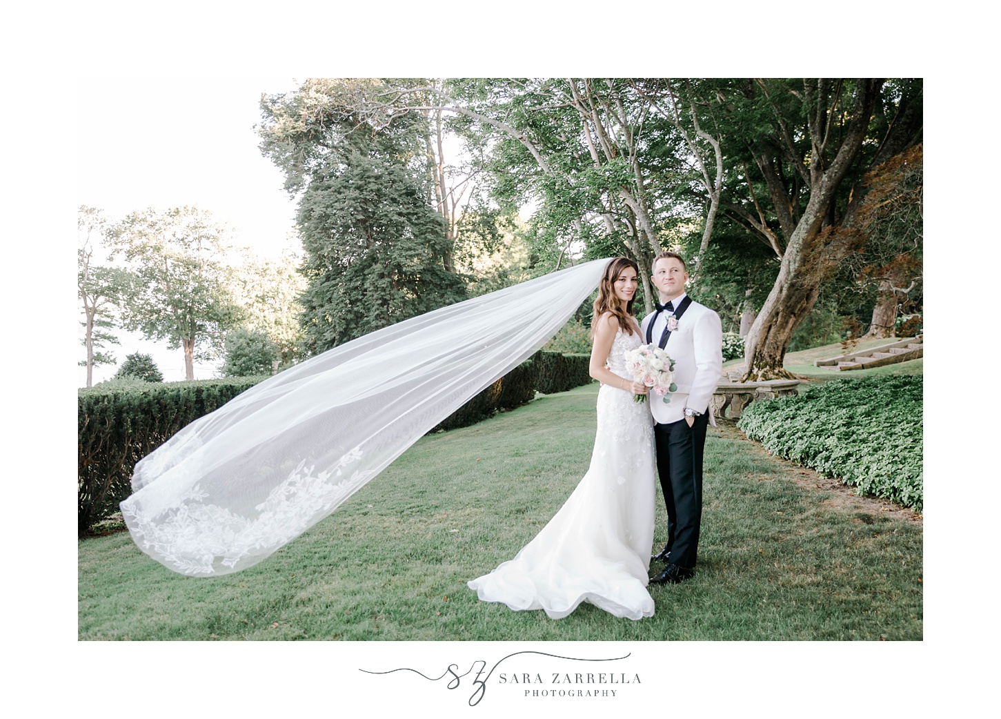 husband and wife pose in gardens of Glen Manor House with bride's veil floating behind her