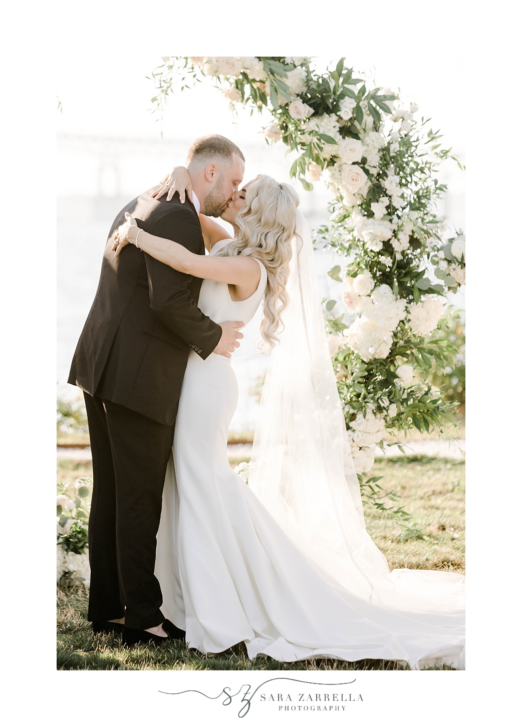 bride and groom kiss by floral arch at Gurney’s Newport Resort