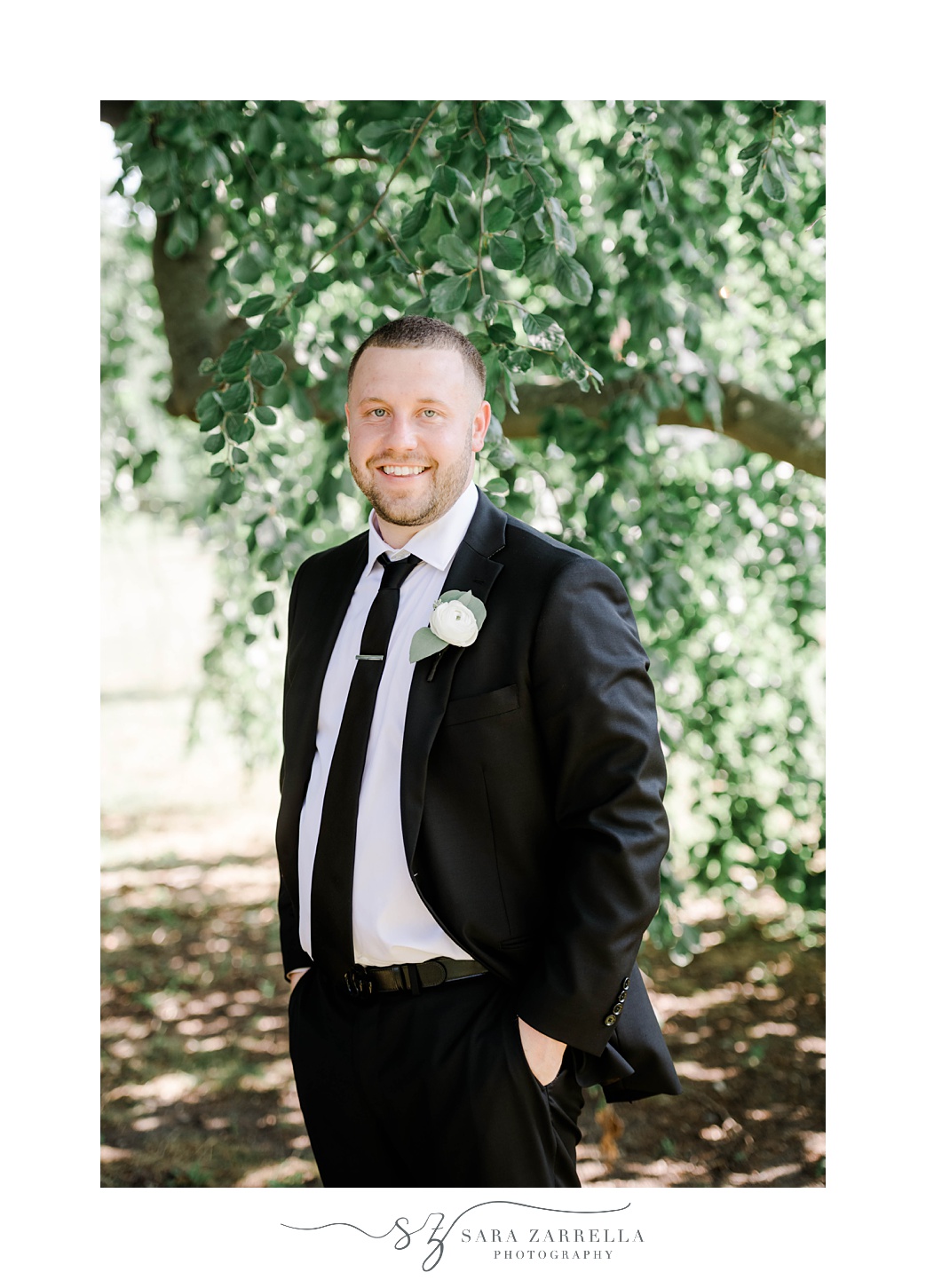 groom smiles with hands in pocket of black suit 