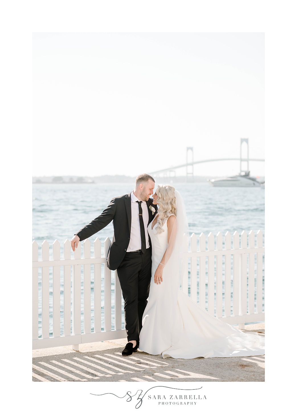 bride and groom kiss by white fence in Newport RI