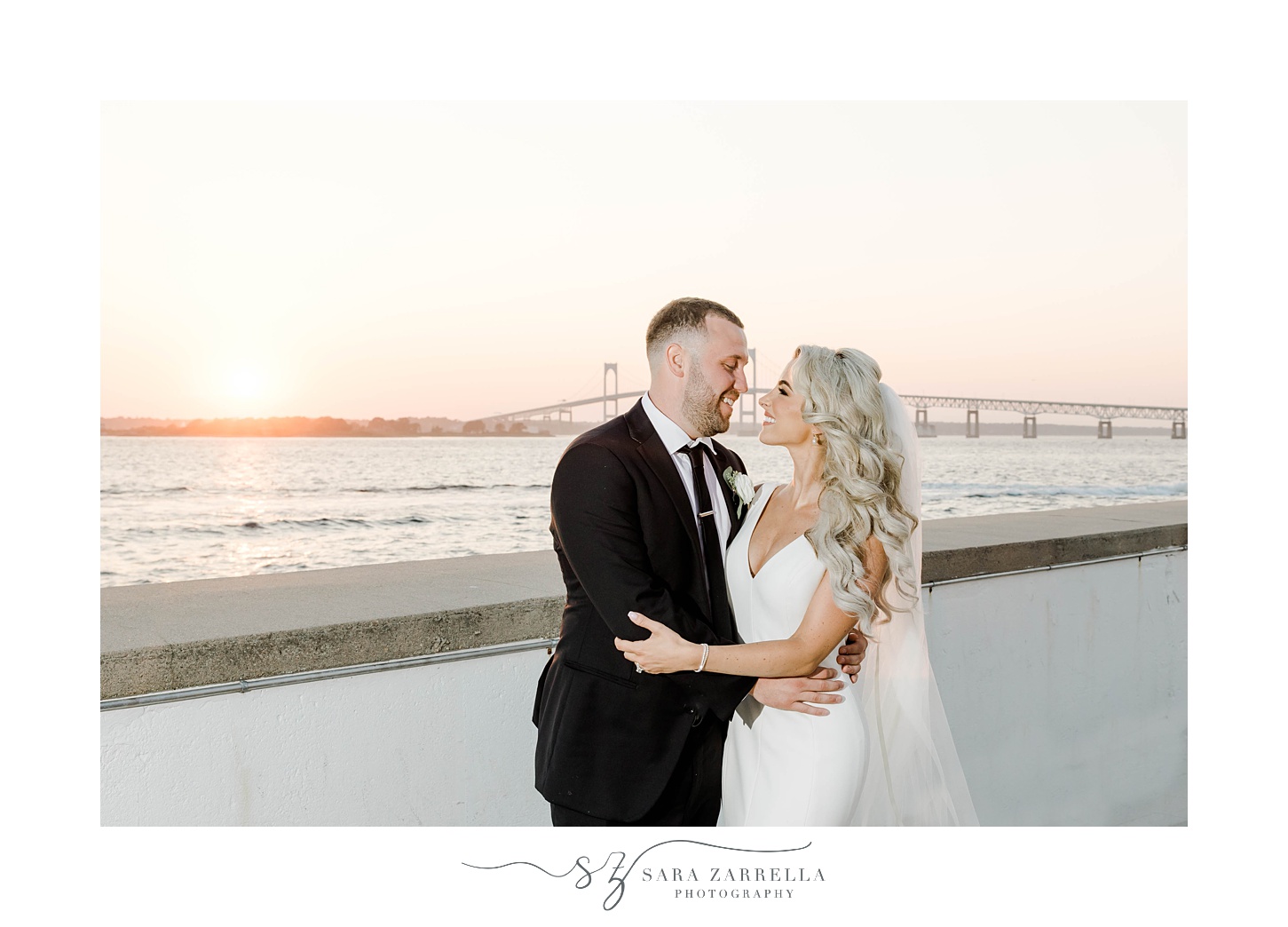 bride and groom hug by Bay at sunset outside Gurney's Newport Resort