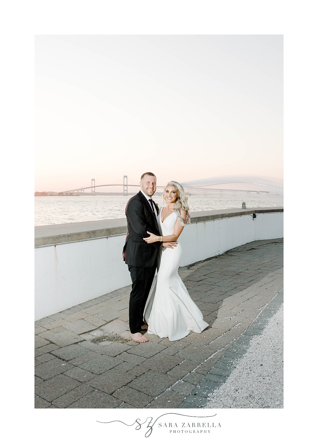newlyweds pose alongside bay outside Gurney's Newport Resort at sunset