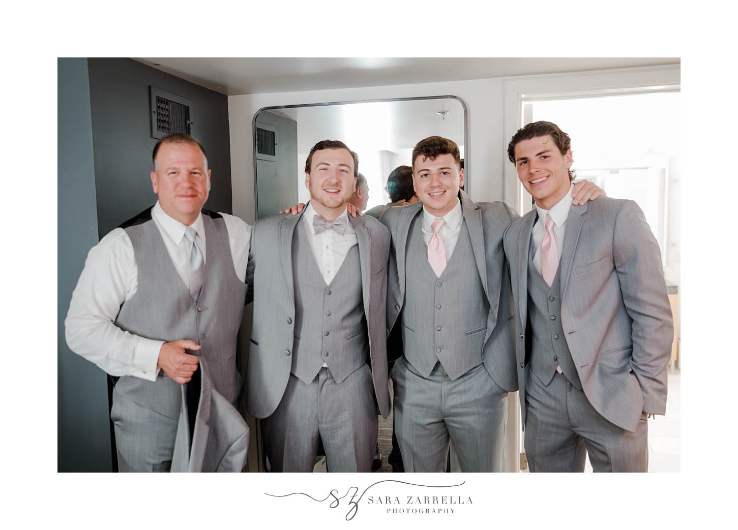 groom stands with groomsmen in grey suits with pink ties