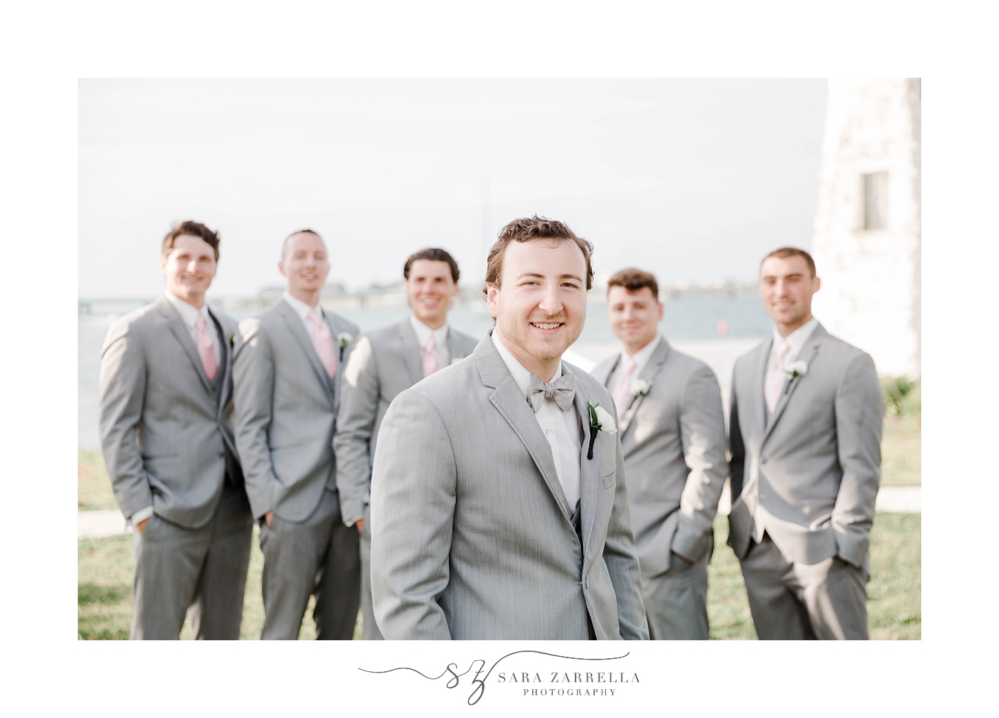 groomsmen in grey suits pose behind groom at Gurney’s Newport
