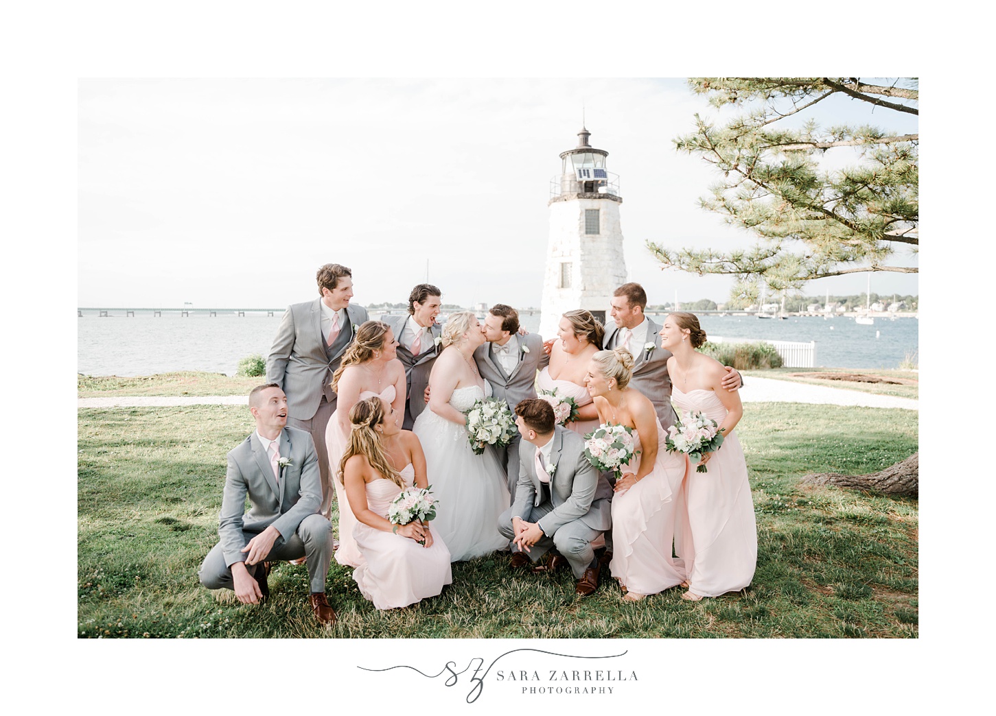 wedding party leans around bride and groom near lighthouse 