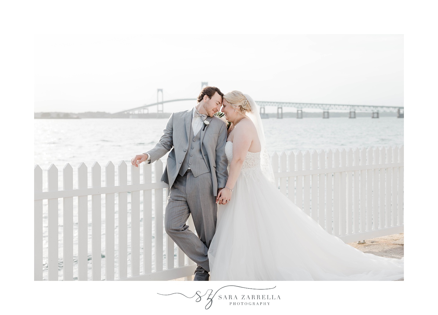bride and groom touch noses with Newport bridge behind them