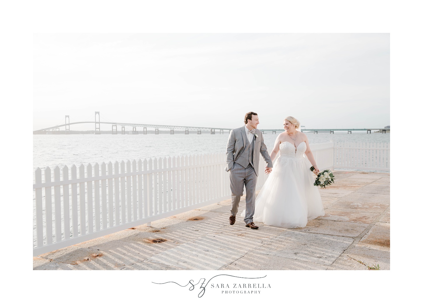 bride and groom hold hands walking by fence in Newport RI