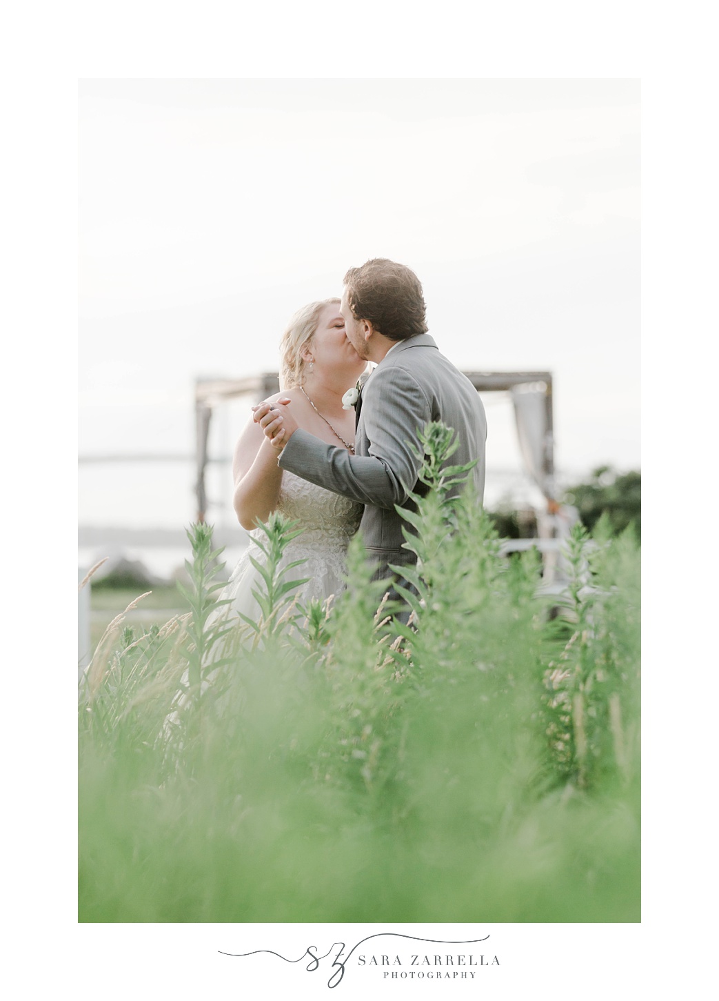 bride and groom kiss in high grass near Gurney’s Newport
