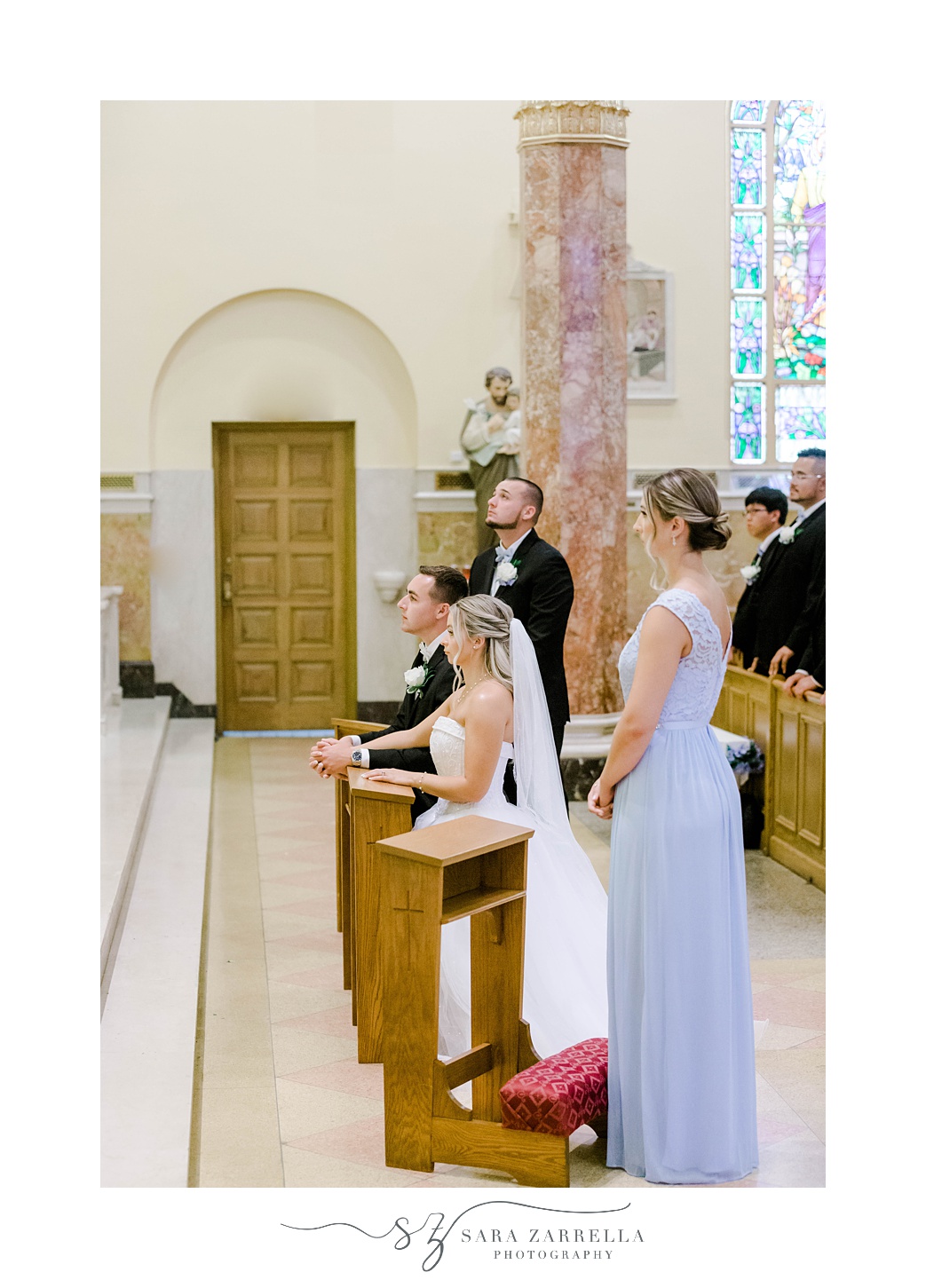 bride and groom kneel with witnesses during Catholic church wedding ceremony in Rhode Island
