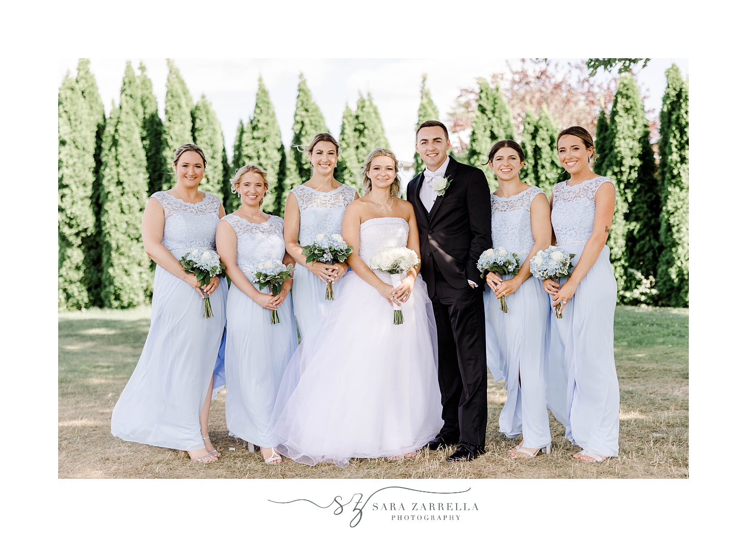 newlyweds stand with bridesmaids in light blue gowns