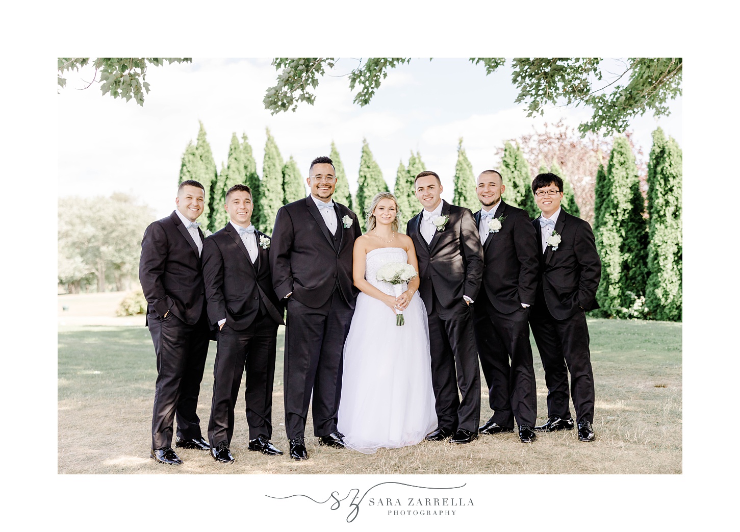 bride stands with groomsmen in black suits