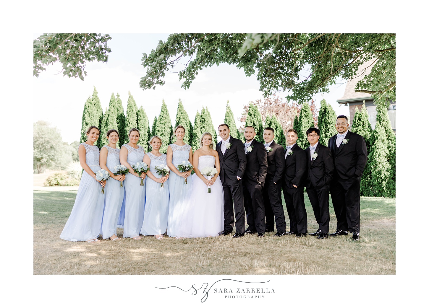 bride and groom pose with wedding party in light blue gowns and black suits