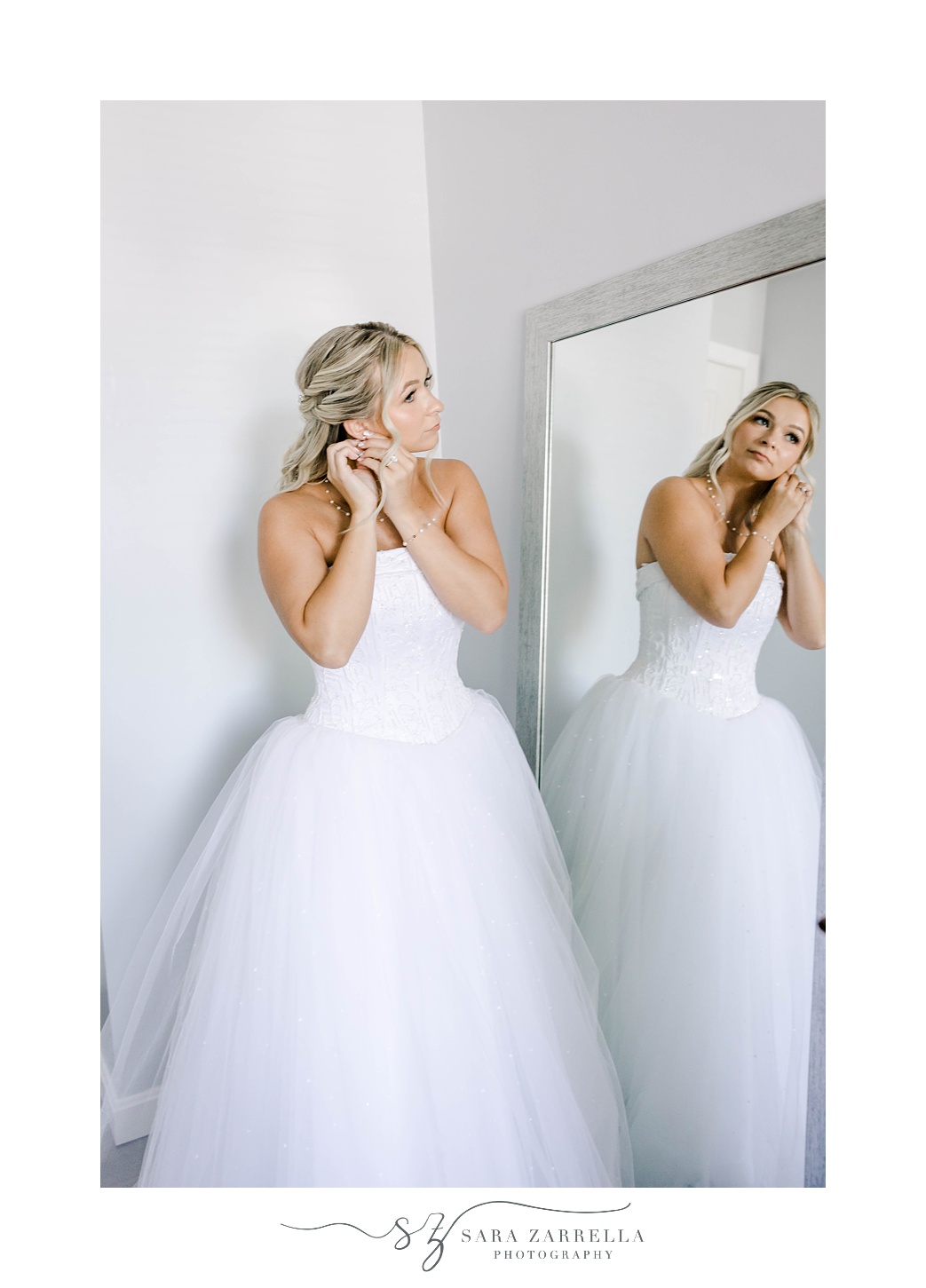 bride puts on earrings in strapless gown