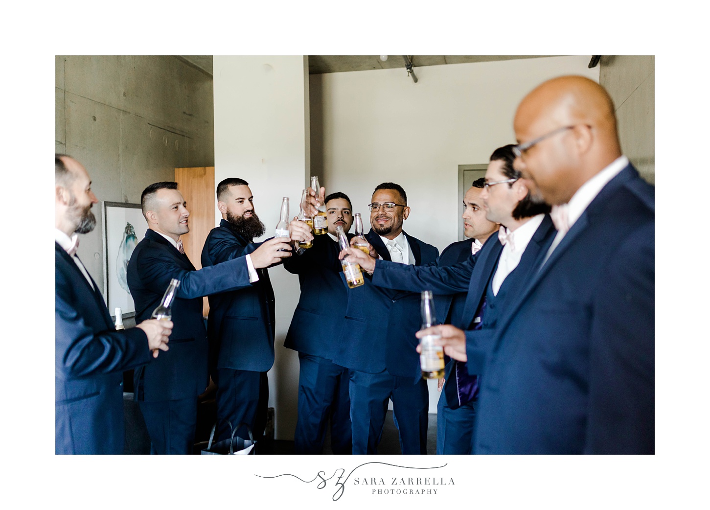 groom and groomsmen in navy suits toast beers