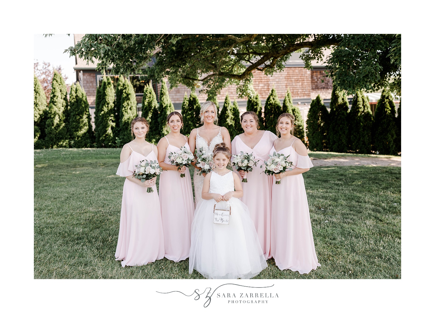 bride poses with bridesmaids in pink dresses with flower girl