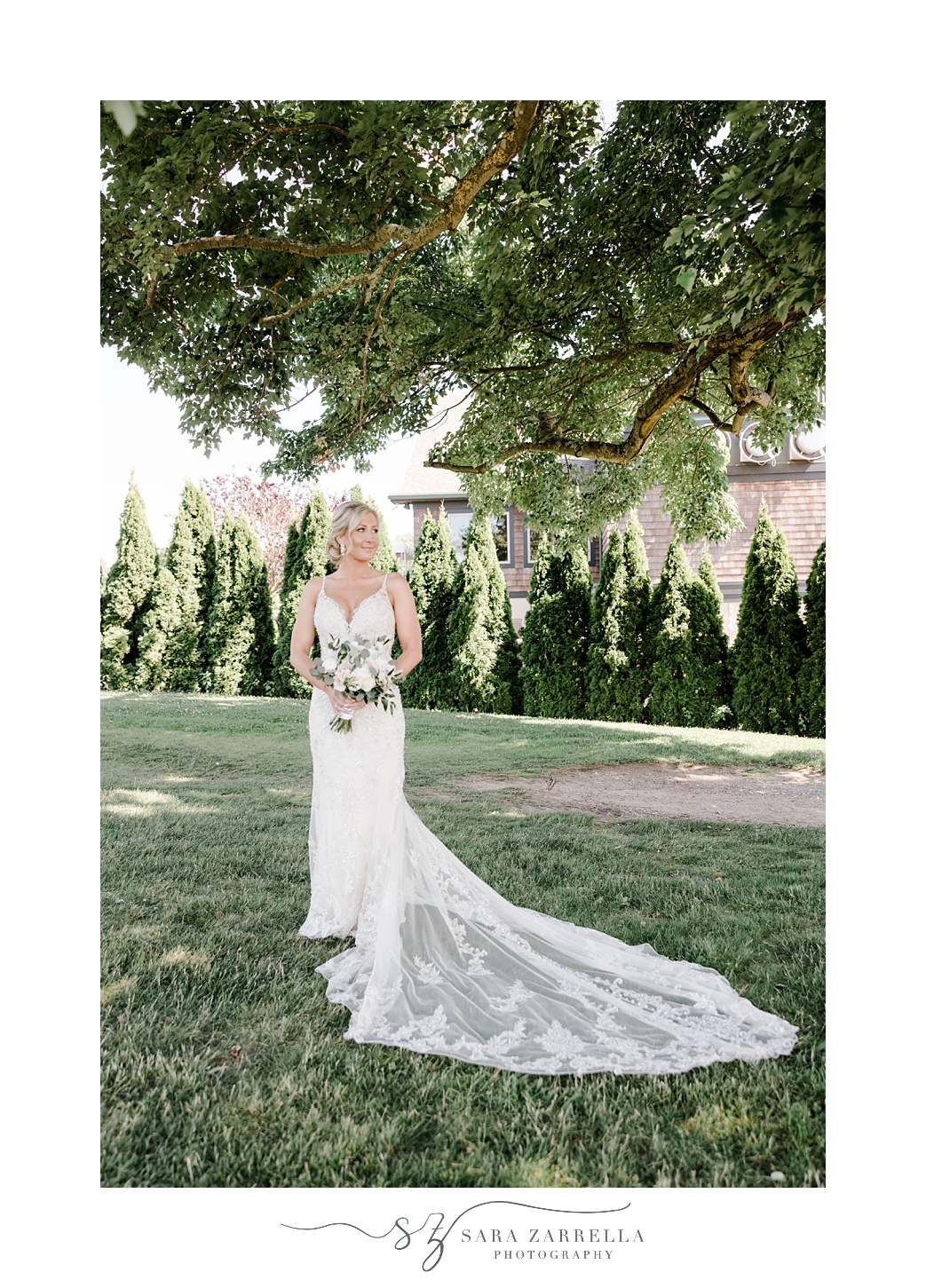 bride stands on lawn at Harbor Lights with lace train of gown around her