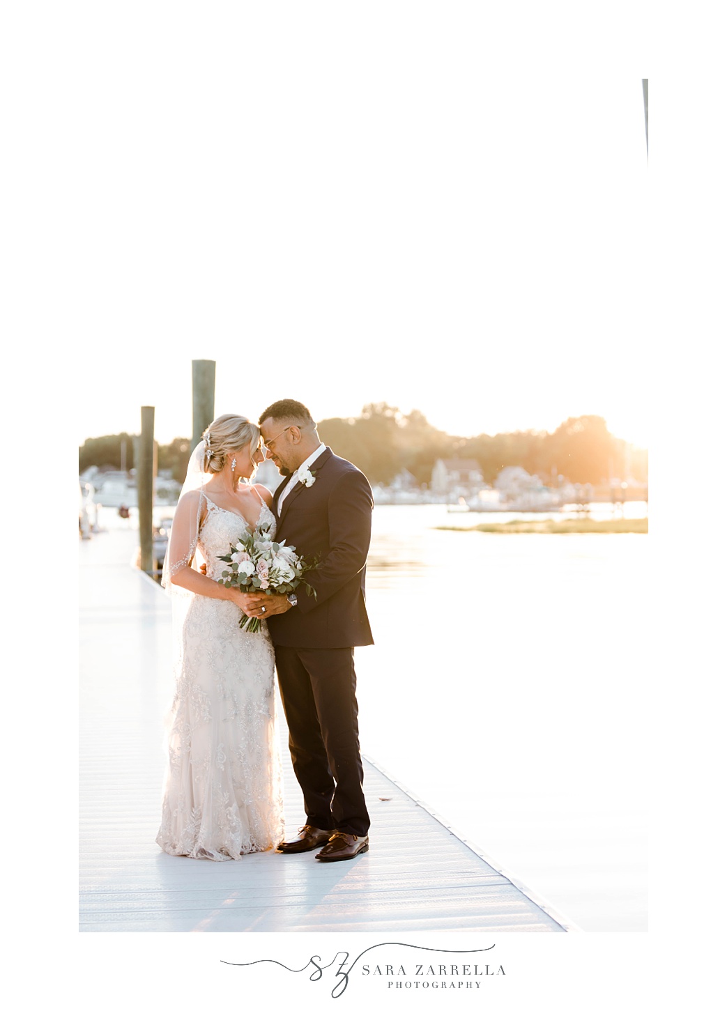 bride and groom hug leaning heads together standing on dock at Harbor Lights