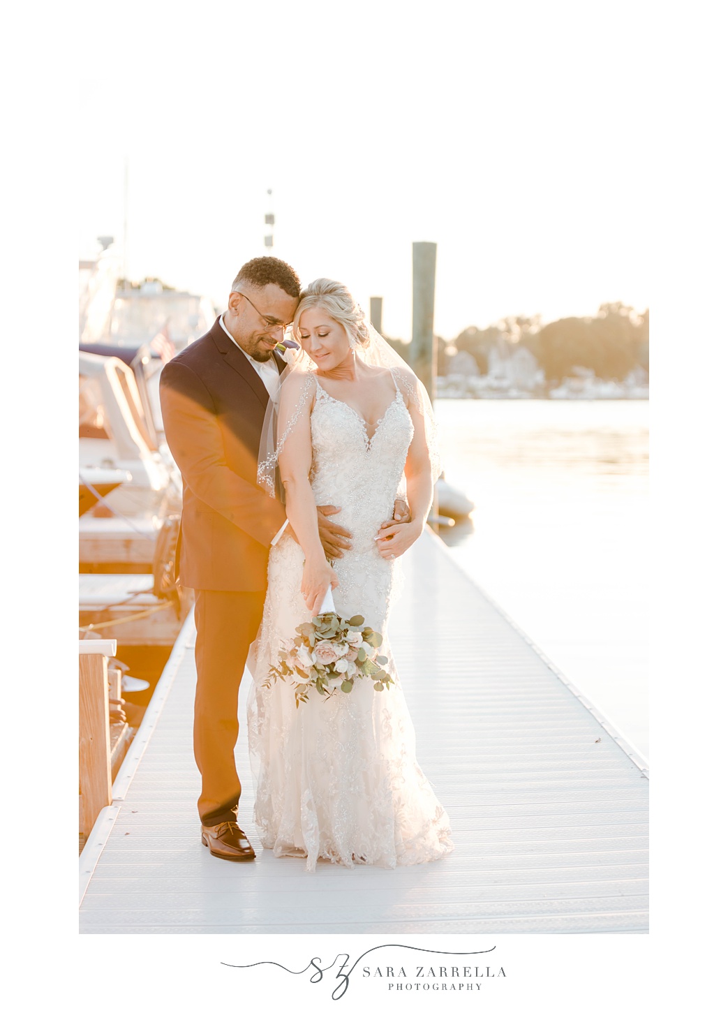 groom stands behind bride kissing her shoulder standing on Harbor Lights dock