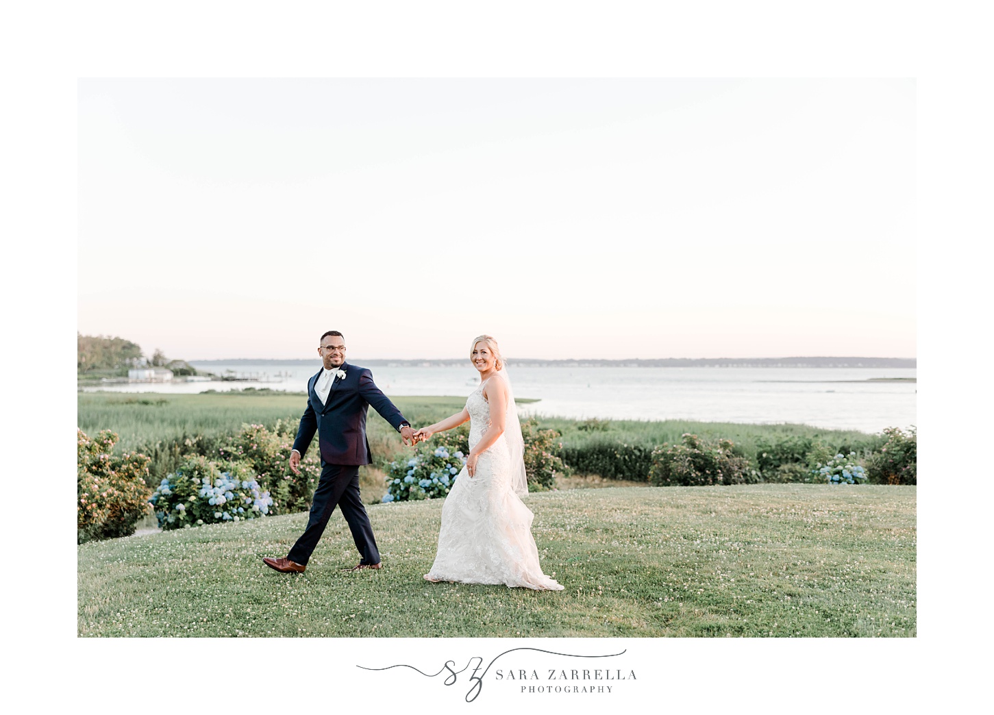 bride and groom hold hands walking along hill at Harbor Lights