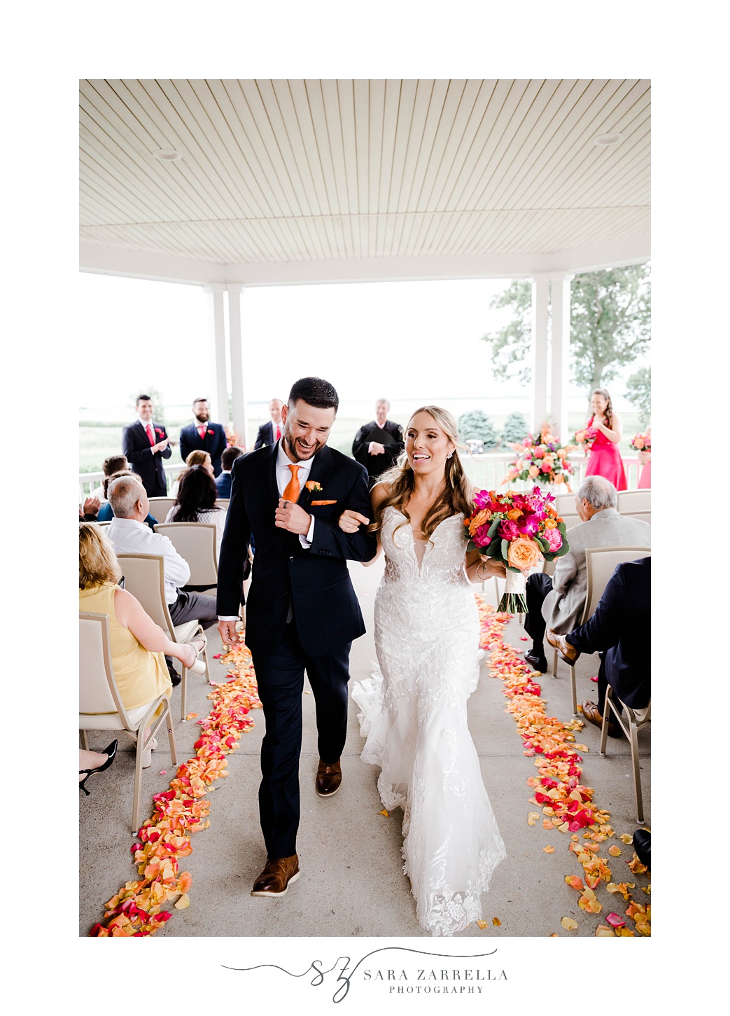 bride and groom laugh walking up aisle lined with pink and orange flower petals