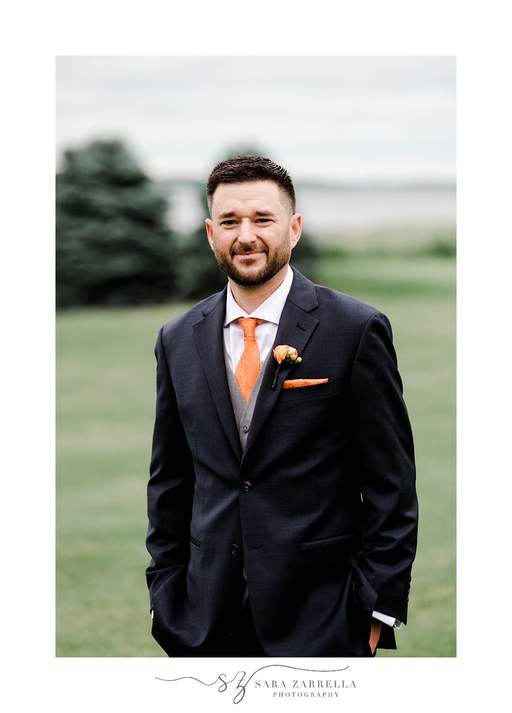 groom stands in black suit with orange tie