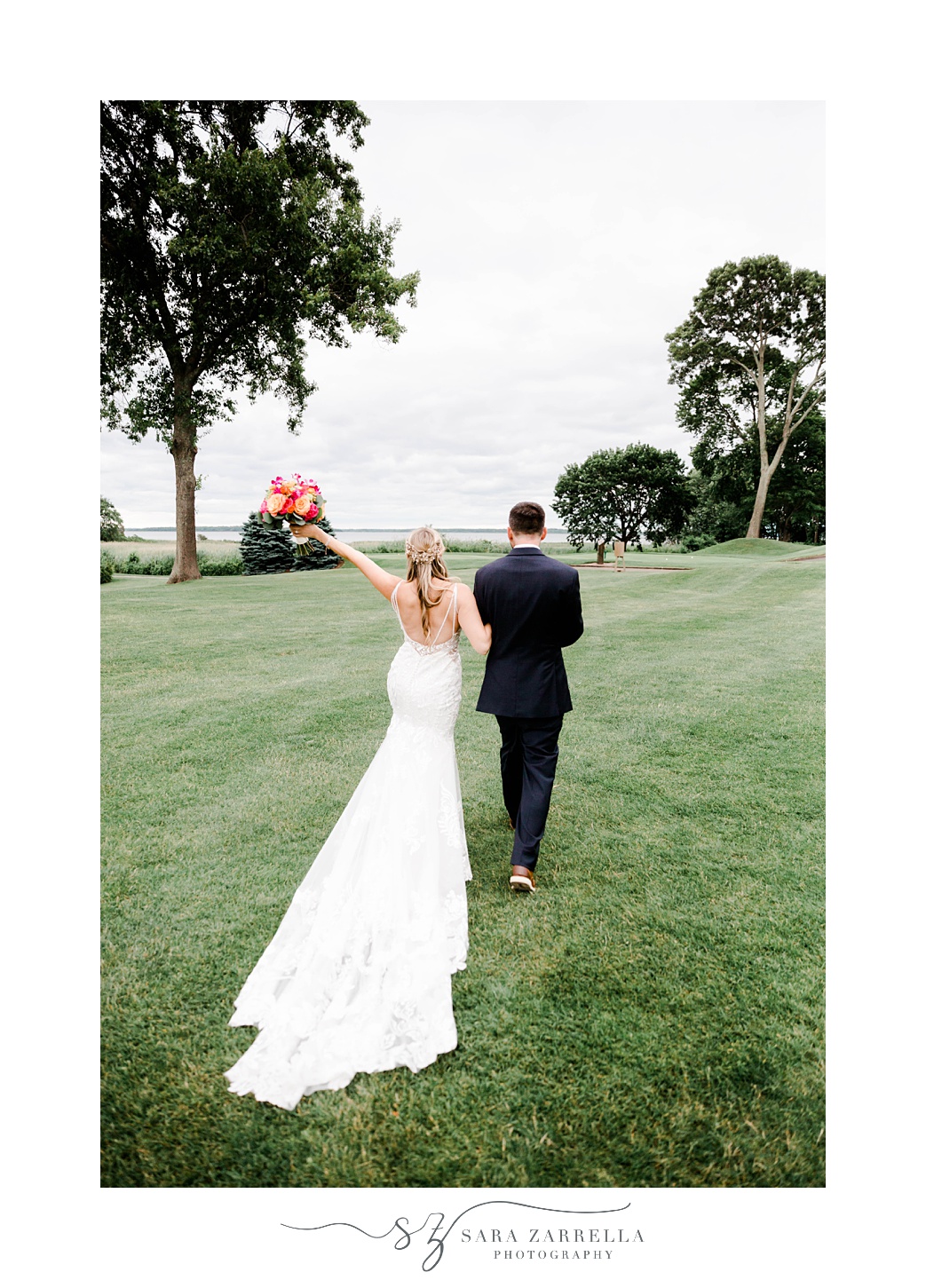 bride and groom walk across lawn while bride holds up bouquet