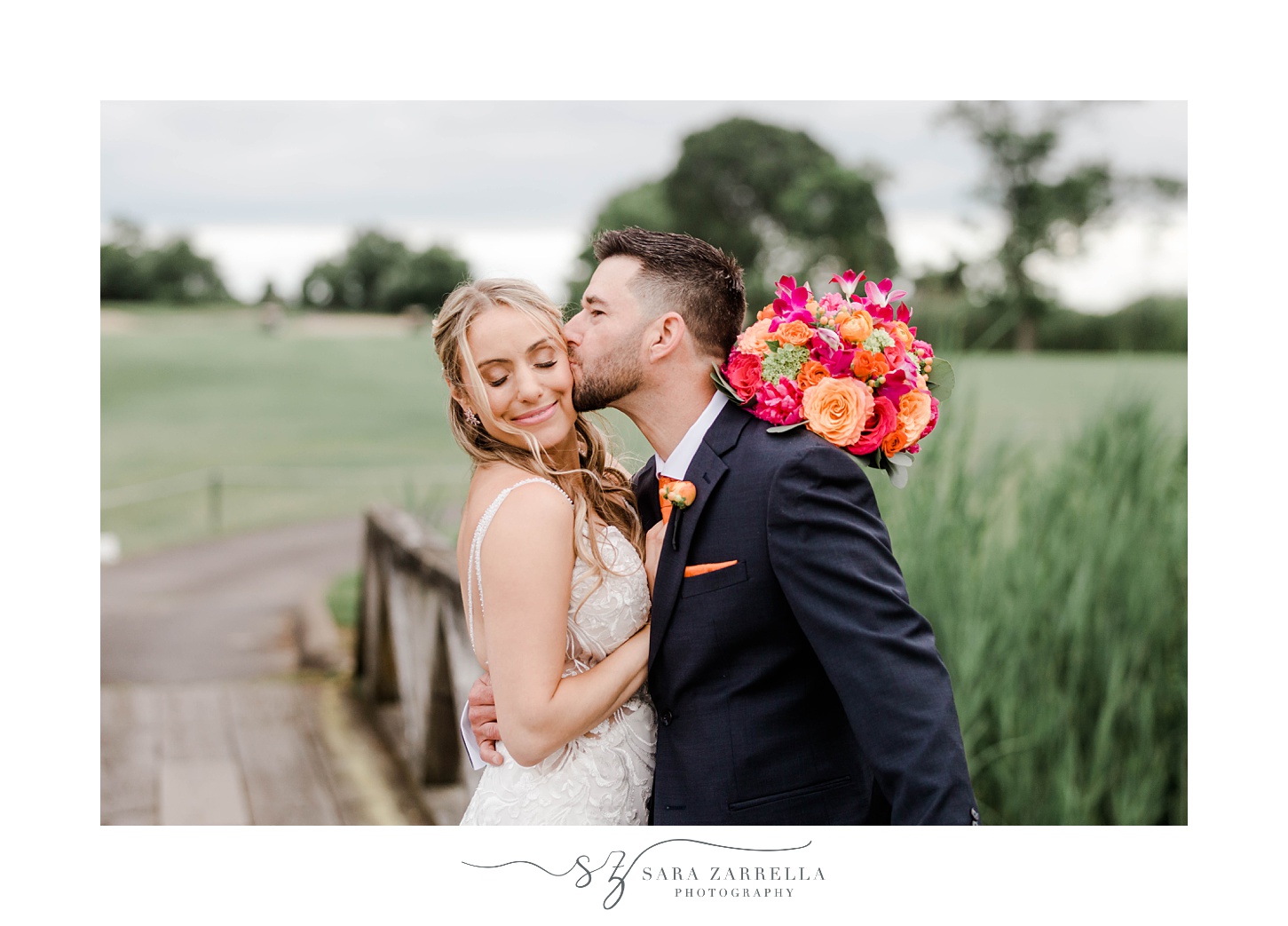 groom kisses bride's cheek during portraits on bridge at Quidnessett Country Club