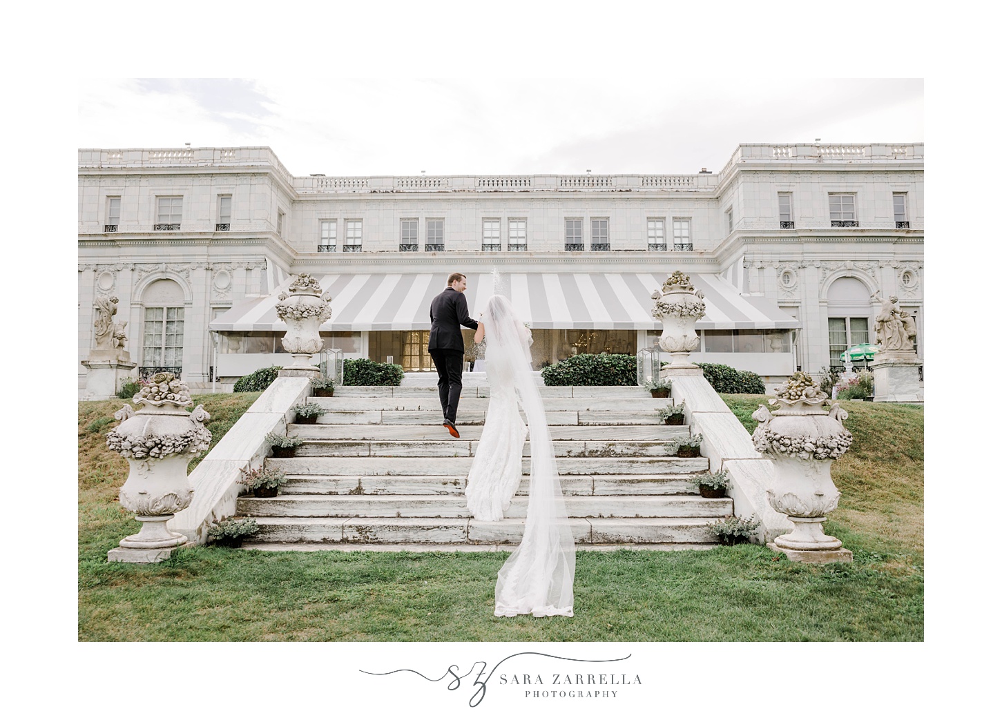 groom helps bride up steps outside Rosecliff Mansion
