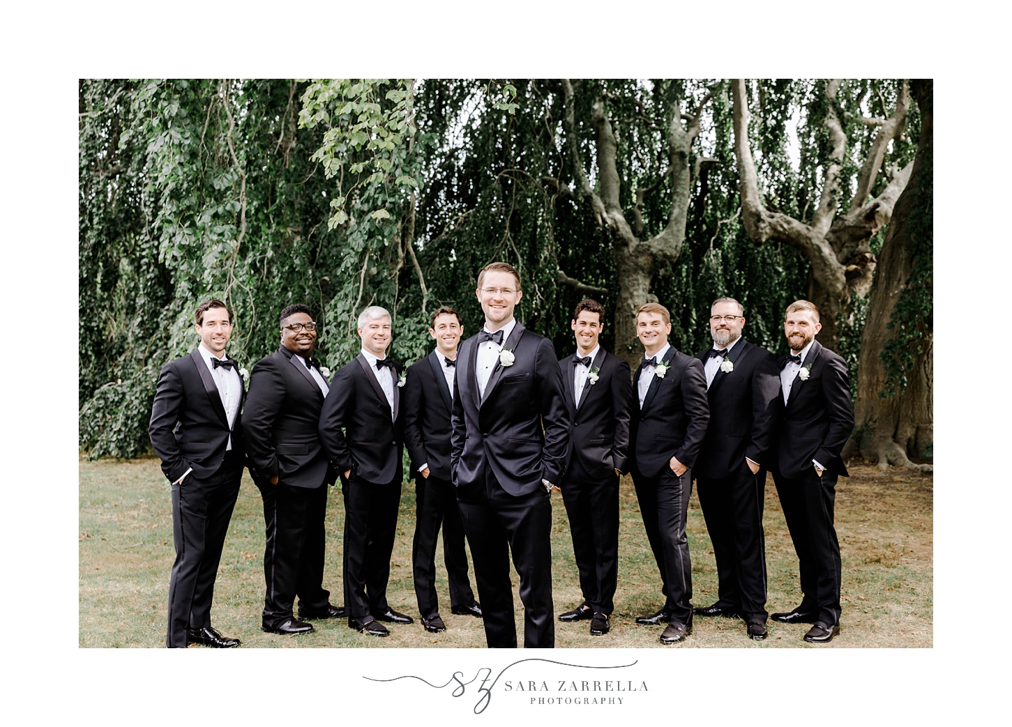groom stands in front of groomsmen in black suits