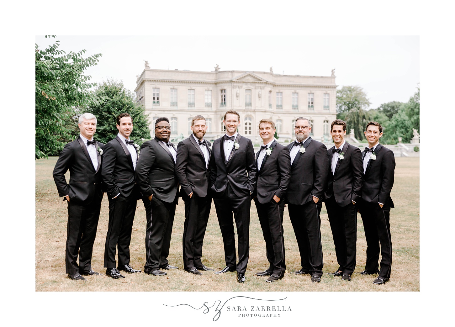 groom and groomsmen stand in line on lawn of The Elms in black suits