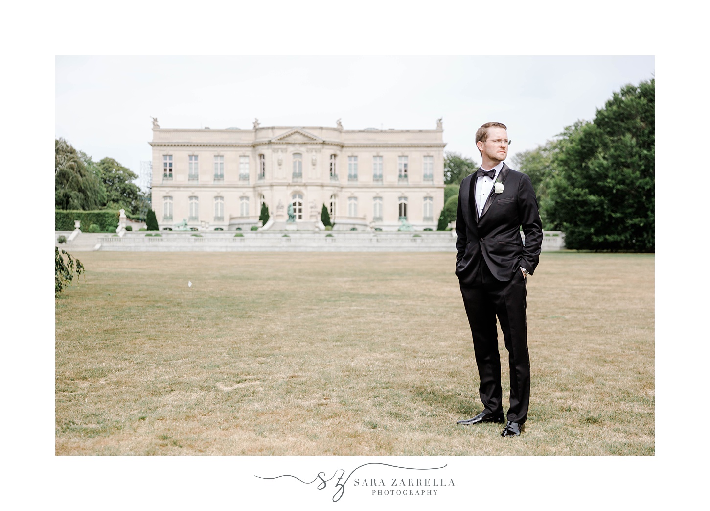 groom in classic suit stands on lawn by manor at The Elms