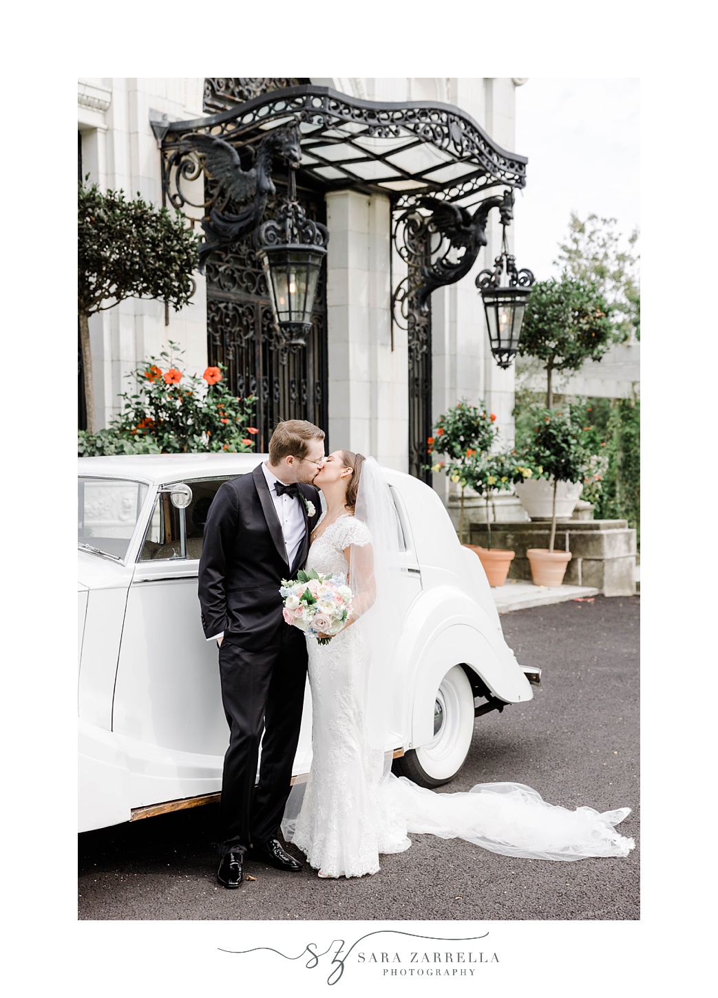 newlyweds kiss by side of white classic car