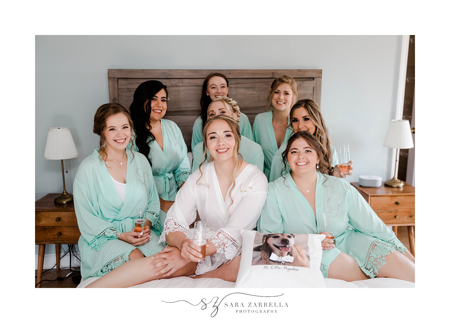 bride sits on bed with bridesmaids in matching teal robes