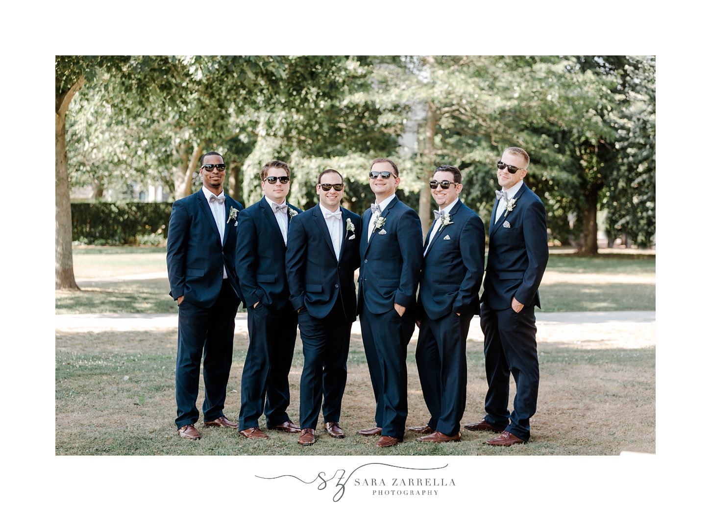 groom and groomsmen stand in navy jackets with sunglasses 