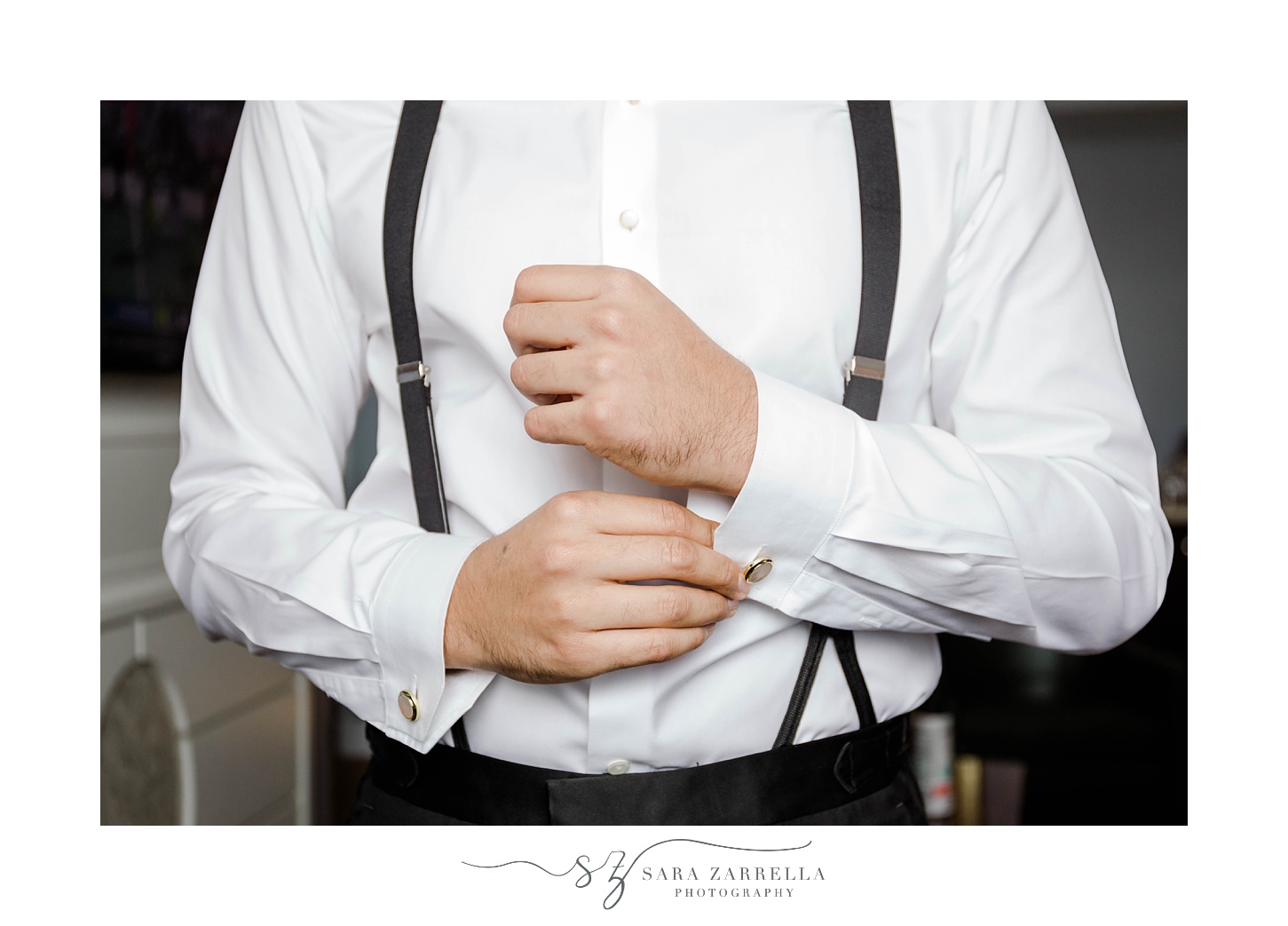 groom stands in white shirt with suspenders adjusting cufflinks