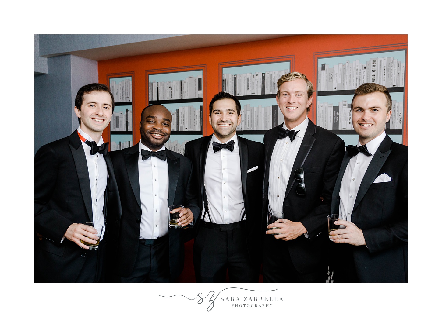 groom stands with groomsmen in classic tuxes in room with orange wallpaper 