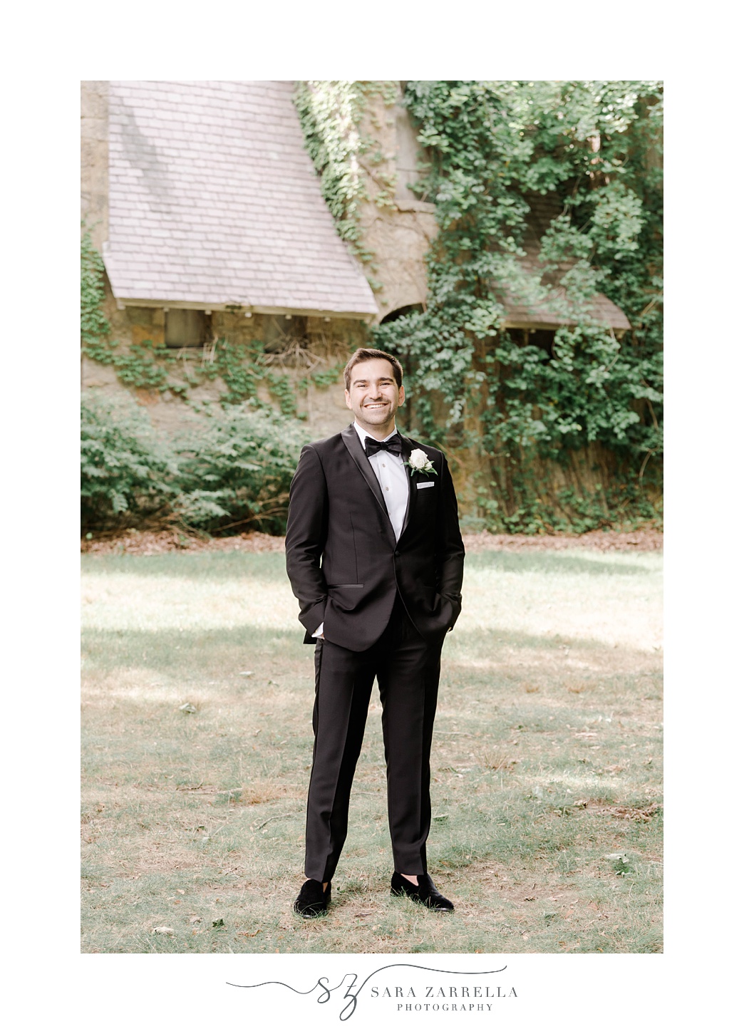 groom stands on lawn at Aldrich Mansion with hands in pocket