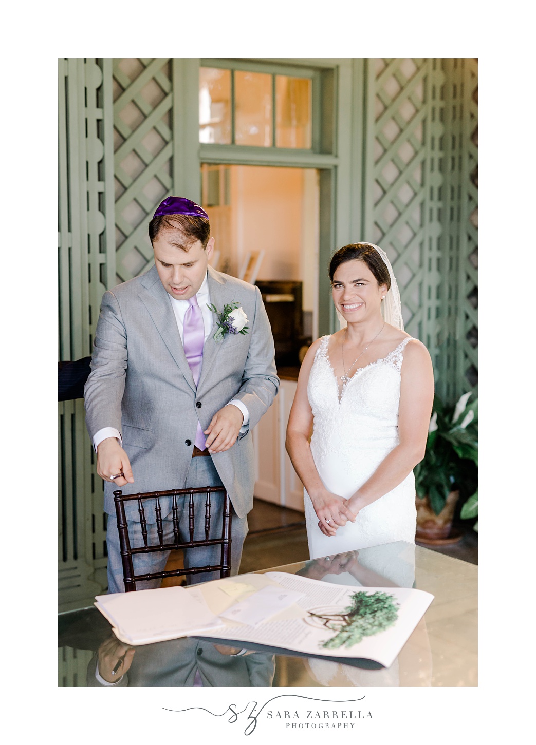 bride smiles while groom reads at Blithewold Mansion