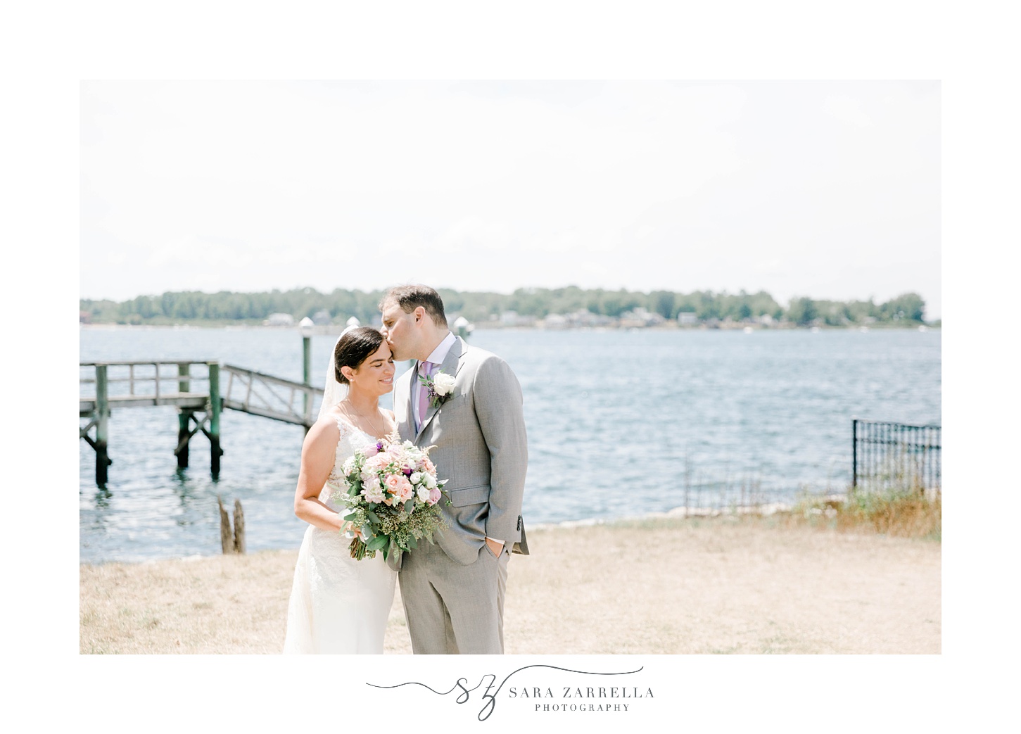 groom leans to kiss bride's forehead during portraits along water in Jewish wedding ceremony at Blithewold Mansion
