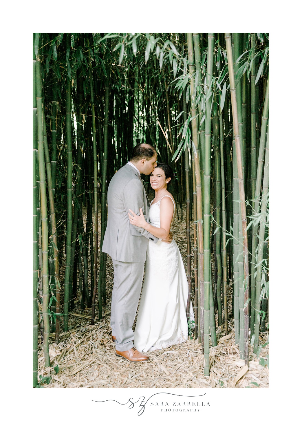 groom leans to kiss bride's forehead among bamboo at Jewish wedding ceremony at Blithewold Mansion
